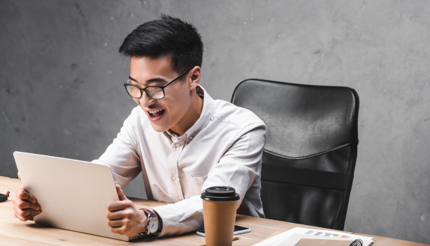 Asiático feliz mientras mira una laptop en Agencia de SEO en Albacete