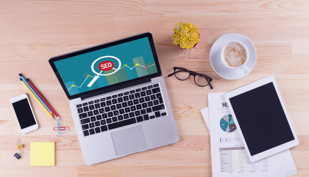 Vista superior de un escritorio con una laptop mostrando un gráfico de SEO en la pantalla, rodeada de una tablet, un smartphone, gafas, una taza de café y documentos con análisis de marketing. Concepto relacionado con Agencia de SEO en Las Palmas de Gran Canaria
