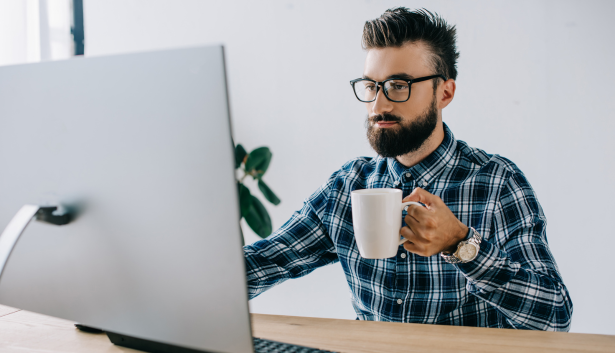 Hombre sujetando una taza mientras mira una mac en Agencia de SEO en San Cristóbal de La Laguna