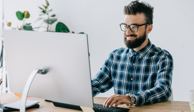 Joven profesional de SEO sonriendo mientras trabaja en una computadora, simbolizando éxito y profesionalidad en servicios de posicionamiento web, identificable con una agencia SEO en Santa Cruz de Tenerife.