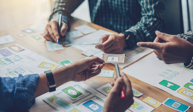 Equipo de profesionales colaborando en el diseño de una interfaz de usuario con esquemas visuales y wireframes, reflejando la estrategia de una agencia de SEO en Tarragona.