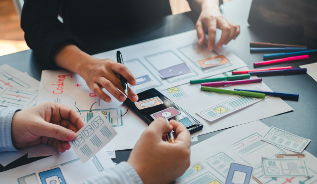 Grupo de profesionales diseñando una interfaz de usuario para una aplicación móvil, organizando elementos visuales y estrategias de experiencia de usuario, representando el enfoque creativo de una agencia de SEO en Valencia.