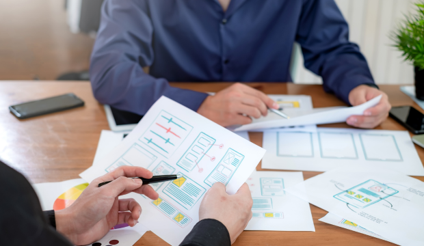 Dos especialistas en marketing digital analizando esquemas de diseño y estrategias de optimización web en una mesa de trabajo, reflejando la planificación y desarrollo de una agencia de SEO en Valencia.