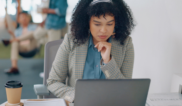Mujer profesional con cabello rizado, vestida con blazer y concentrada mientras trabaja en su laptop en un entorno de oficina moderna, reflejando la estrategia y análisis en una agencia de SEO en Vitoria-Gasteiz.