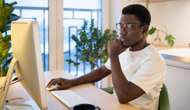 Joven profesional con gafas y camiseta blanca trabajando en su computadora de escritorio en un espacio moderno con plantas, reflejando el análisis y optimización web en una agencia de SEO en Zaragoza.